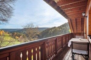 A wooden balcony with a table and chair, overlooking a mountainous landscape.