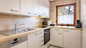 A modern kitchen with a Bosch dishwasher, a microwave, a coffee maker, and a window with a view of trees. - Apartment 'Wiesenblick' with Shared Terrace, Shared Garden and Wi-Fi (Schramberg)