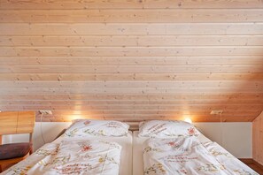 A room with two beds, wooden ceiling, a chair, and a wall socket.