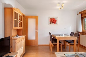 A room with a wooden dining table, chairs, a cabinet with glass doors, a door, a framed picture on the wall, and a window with curtains. - Apartment 'Gartenblick' with Shared Terrace, Shared Garden and Wi-Fi (Schramberg)
