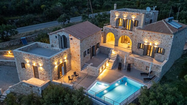 Une villa en pierre dotée d’une piscine, d’un espace salon extérieur et de plusieurs balcons.