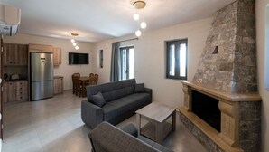 Un salon moderne avec une cheminée en pierre, un canapé gris, un coin repas avec un téléviseur et une cuisine équipée d’un réfrigérateur intégré.