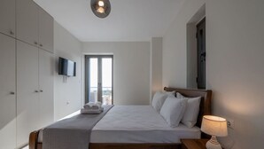 Une chambre à coucher comprenant un lit, une table de chevet, une lampe, une télévision, une armoire et une fenêtre donnant sur un beau paysage.