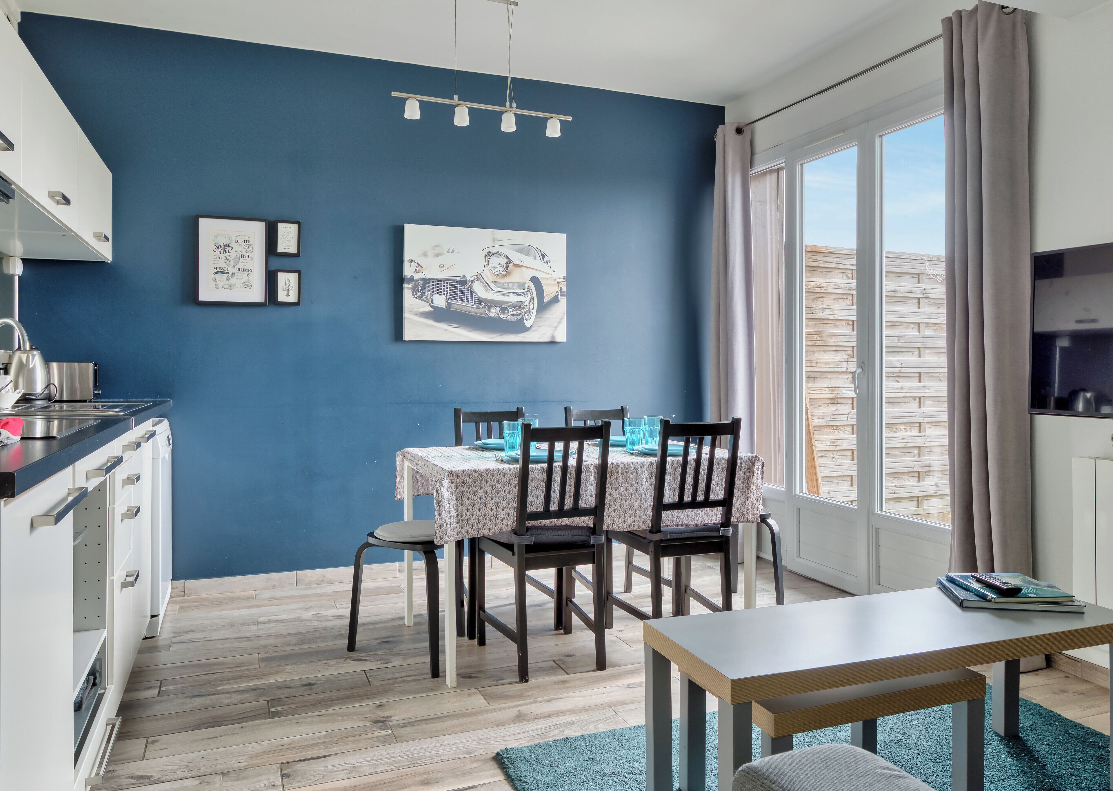 Une cuisine moderne avec un mur bleu, un plancher en bois et un coin repas comprenant une table et des chaises.