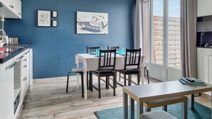 A modern kitchen with a blue wall, wooden flooring, and a dining area with a table and chairs. - Le Léon Gambetta, appartement avec terrasse vue mer (Dieppe)