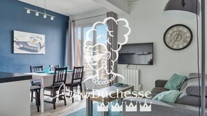 A modern living room with a dining area, a large window, and a flat-screen TV mounted on the wall. - Le Léon Gambetta, appartement avec terrasse vue mer (Dieppe)