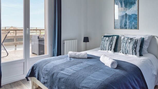 A bedroom with a large bed, a view of the outdoors, a painting on the wall, and a radiator. - Le Léon Gambetta, appartement avec terrasse vue mer (Dieppe)