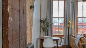 Una sala de estar moderna con una pared de ladrillo, un comedor con mesa y sillas, y un sofá con vista a la calle.