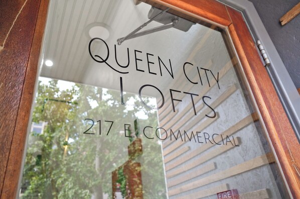 A window with the text "QUEEN CITY LOFTS 217 E. COMMERCIAL" and a view of trees outside.