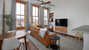 Una sala moderna con sofá, televisión, mesa de comedor y ventanas amplias.