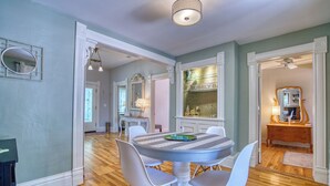 A dining area with a round table, white chairs, and a chandelier. There is a mirror on the wall and a ceiling fan. - Craftsman Oasis in Old Longmont (Longmont)