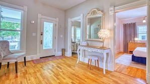 A spacious room with hardwood flooring, a white chair, a vanity with a mirror, and a bed. - Craftsman Oasis in Old Longmont (Longmont)