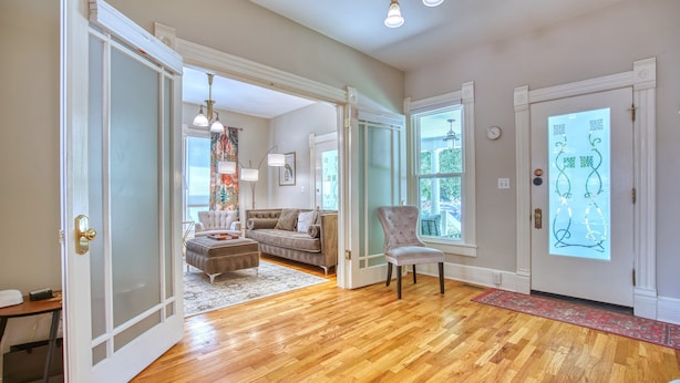 An open door leading to a living room with a wooden floor, a grey armchair, a sofa, and a rug. - Craftsman Oasis in Old Longmont (Longmont)