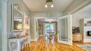 A spacious hallway with hardwood flooring, a white console table, a mirror, and a dining area with chairs and a table. - Craftsman Oasis in Old Longmont (Longmont)