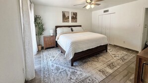 Un dormitorio con cama, mesita de noche, lámpara, ventilador de techo y una alfombra grande.