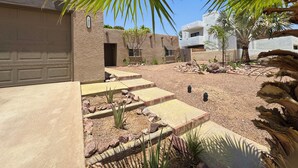 Una zona residencial con garaje, entrada pavimentada y un pequeño jardín con rocas y plantas.
