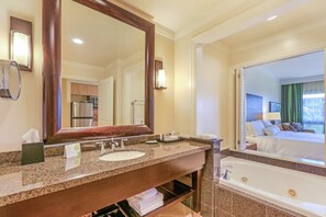 A hotel bathroom with a large mirror, two sinks, a vanity, and a bathtub.