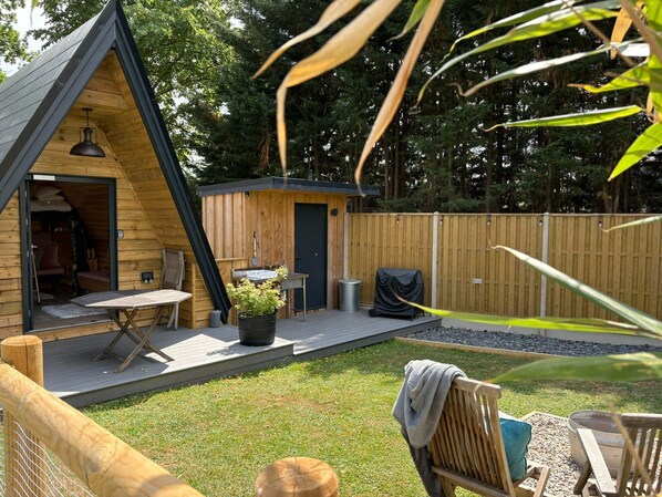 Een houten A-frame hut met een terras, een kleine tafel en een bankje.