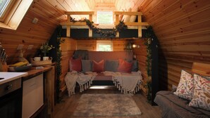 Un interior de cabaña acogedor con cama en altillo, una kitchenette pequeña y un ventanal que proporciona luz natural.