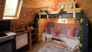 Interior acogedor de una cabaña con techo de madera, un sofá con cojines, un escritorio pequeño y una ventana.