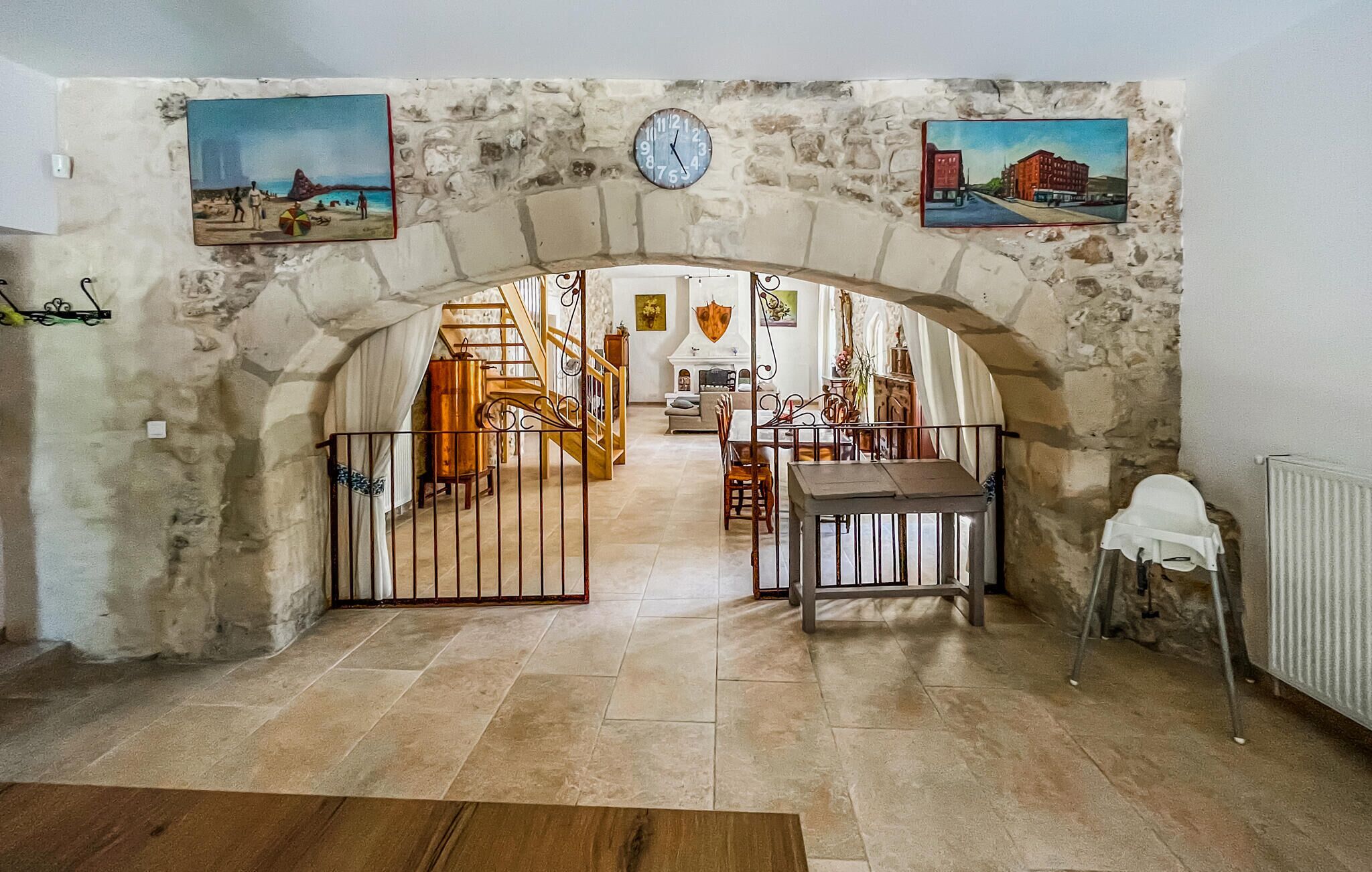 Una porta arquejada que condueix a una zona de dinar amb una taula i cadires, un rellotge a la paret i dos quadres sobre la porta.