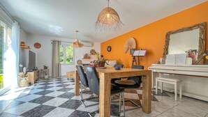 Ein Essbereich mit kariertem Boden, einem Holzesstisch und Stühlen. An der Wand hängt ein großer Spiegel, eine Deckenlampe und ein Fenster mit Vorhängen.
