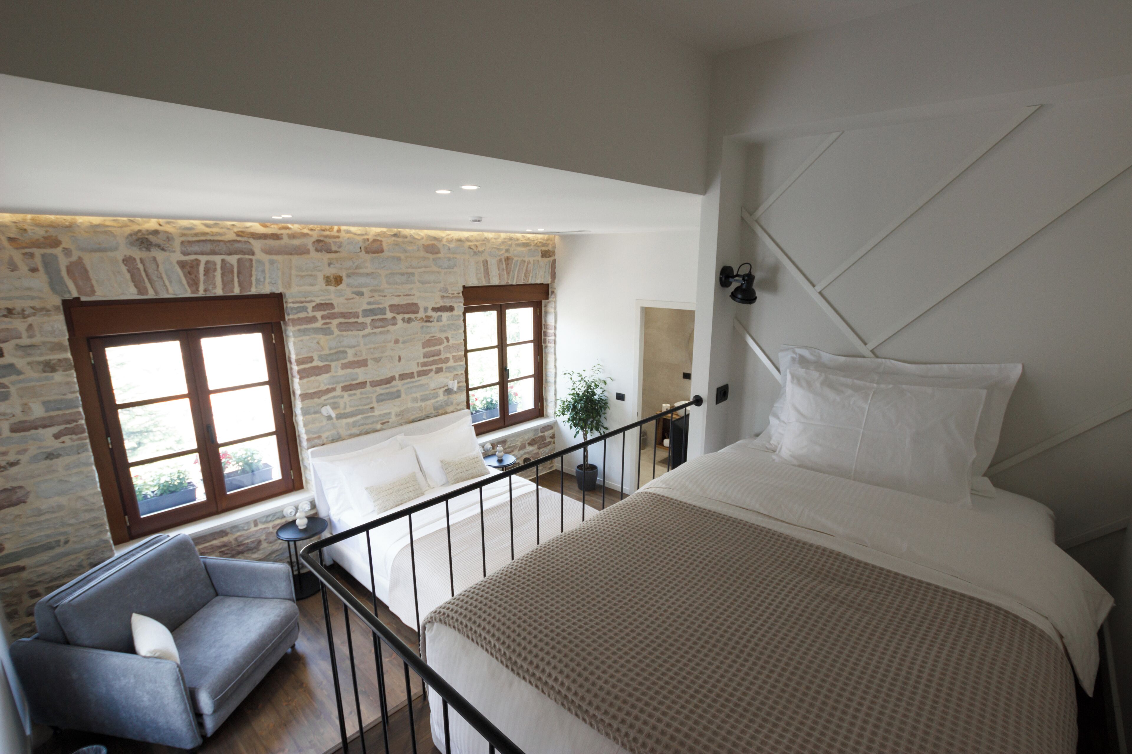 A bedroom with a large bed, a stone wall, and a view of the outdoors.