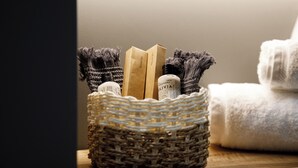 A woven basket containing toiletries on a wooden surface, next to a white towel. - Stitch&Stone Suites (Gjirokastër)