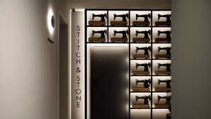 A hallway with a wall displaying multiple sewing machines and a sign reading "STITCH & STONE". - Stitch&Stone Suites (Gjirokastër)