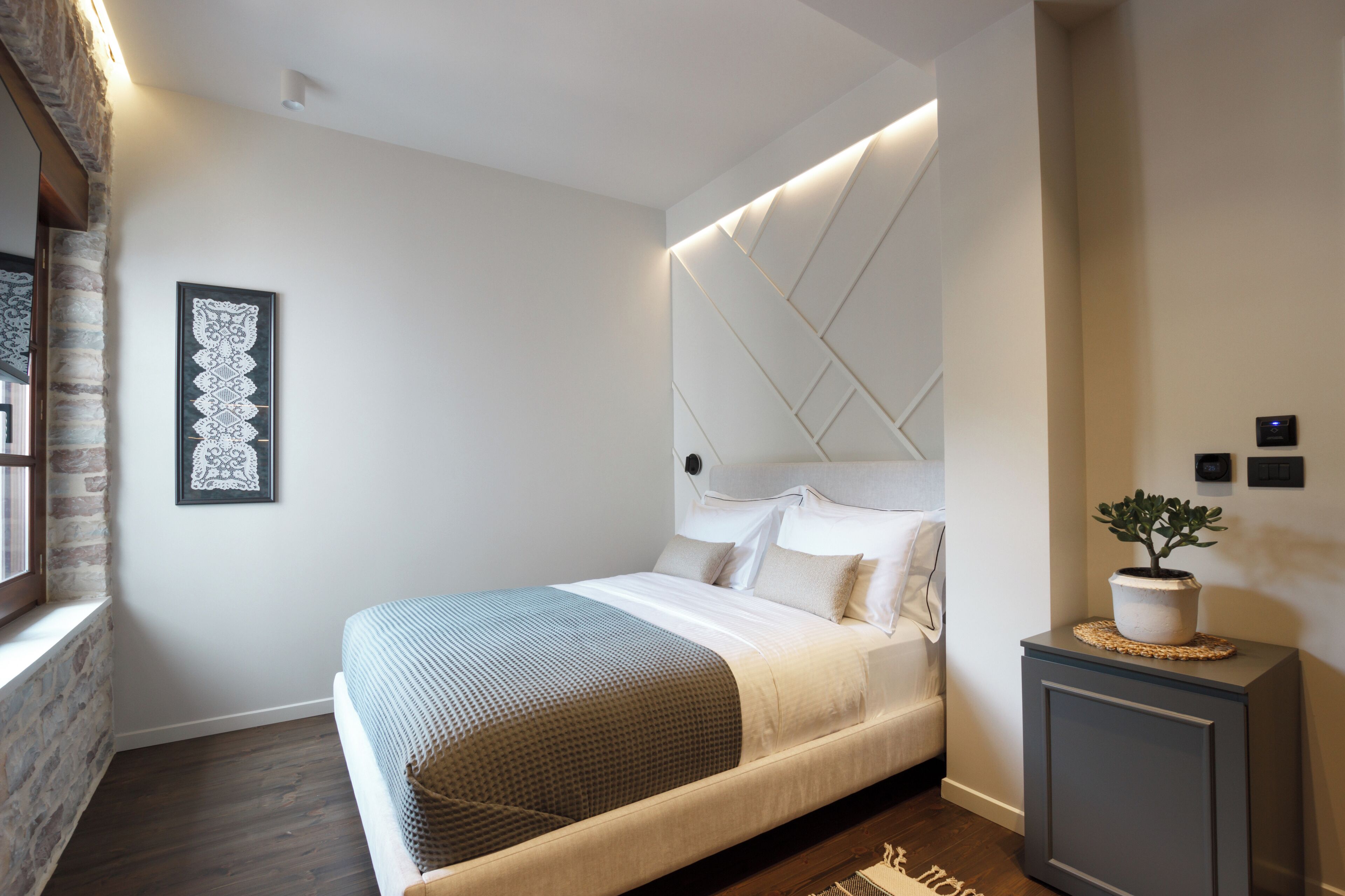 Un dormitorio moderno con una cama grande, un cabecero decorativo, una mesita de noche con una planta y una obra de arte enmarcada en la pared.