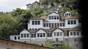 A multi-story building with a traditional architectural style, featuring a mix of stone and plaster exteriors, multiple windows, and a prominent central tower. - Stitch&Stone Suites (Gjirokastër)