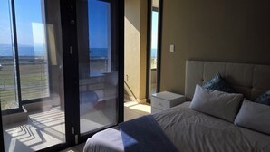 Ein Schlafzimmer mit einem großen Bett, einem Nachttisch und Meerblick durch eine Schiebetür.