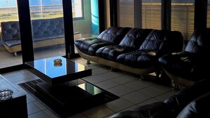 Ein modernes Wohnzimmer mit einer schwarzen Ledersofa, einem Glastisch und großen Fenstern mit Blick auf das Meer.