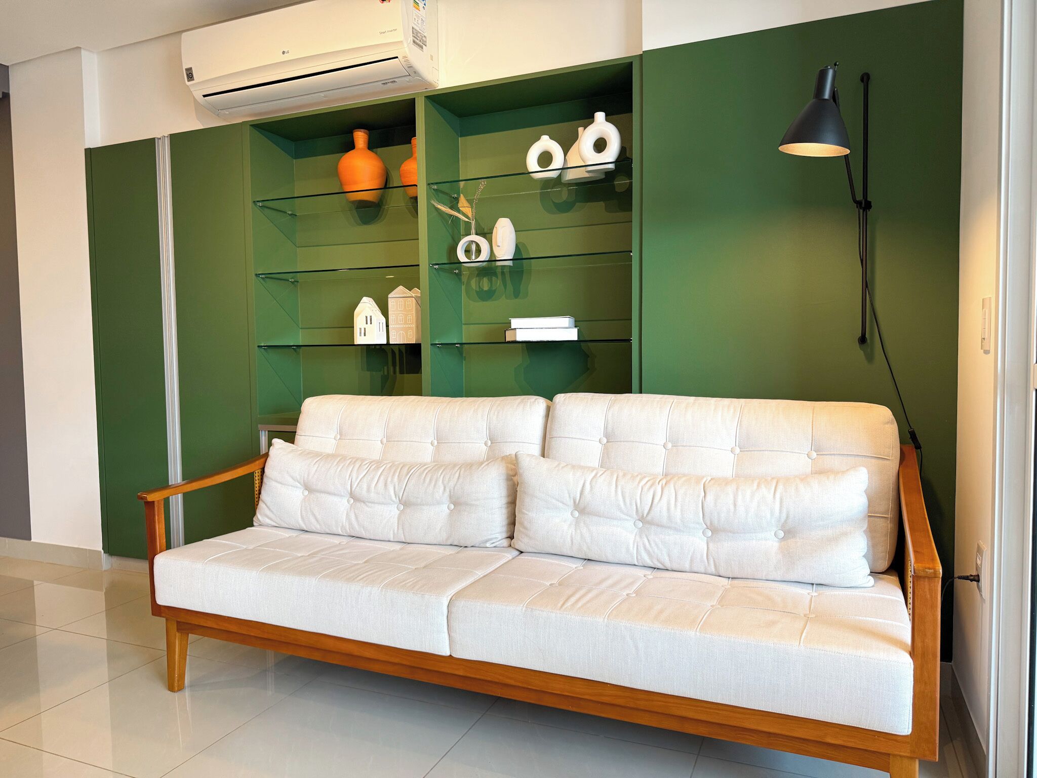 A modern living room with a white sofa, green walls, and a glass shelving unit displaying decorative items.
