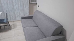 Un sofá gris en una habitación con suelo de baldosas y pared blanca.