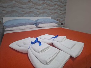 Una cama bien hecha con toallas blancas atadas con cintas azules, una colcha roja y un papel tapiz estampado al fondo.