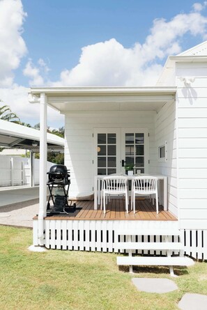 Une terrasse couverte avec un barbecue, des chaises blanches et une table.