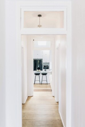 A narrow hallway leading to a kitchen with white cabinets, a black countertop, and two stools. - Urban Getaway Ipswich W Cottage (West Ipswich)