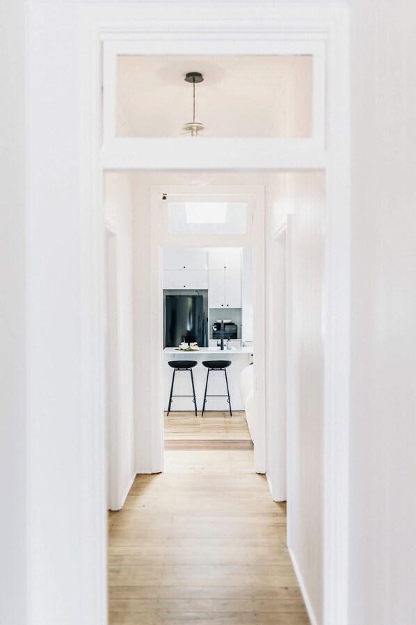 A narrow hallway leading to a kitchen with white cabinets, a black countertop, and two stools.