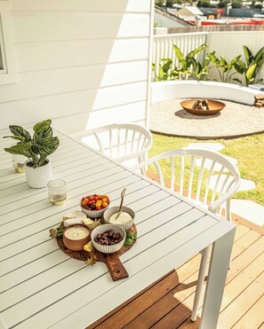 A white wooden deck with a table set for a meal, surrounded by white chairs.