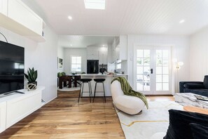 A modern kitchen with white cabinetry, a dining area with a white sofa, and a TV on a white console.