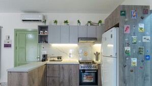 A compact kitchen with a built-in oven, a refrigerator, and a microwave. There are potted plants on the countertop, and the backsplash is made of white tiles with a subtle pattern.