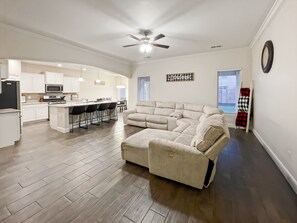 A modern living room with a sectional sofa, a dining area with bar stools, and a kitchen with white cabinetry. - 3-bedroom house in welcoming Hobbs with WiFi, AC (Hobbs)