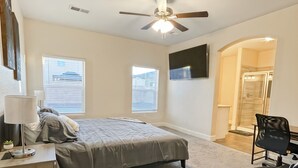 Une chambre avec deux lits, un ventilateur de plafond, un bureau avec une lampe, une chaise et une grande fenêtre.
