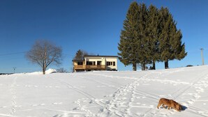 Een huis met een balkon, omgeven door sneeuw en bomen.