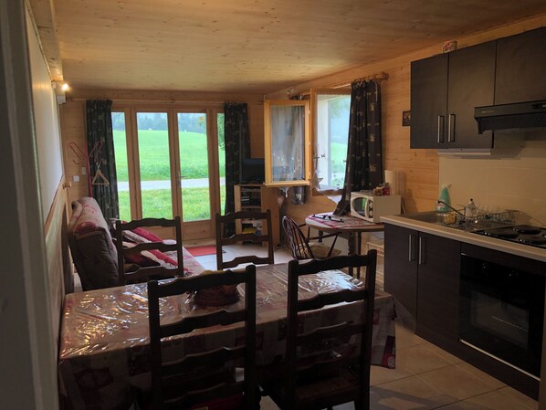 Eine gemütliche Küche mit Holdekor, einem Esstisch mit Stühlen und Blick auf ein grünes Feld durch die Fenster.