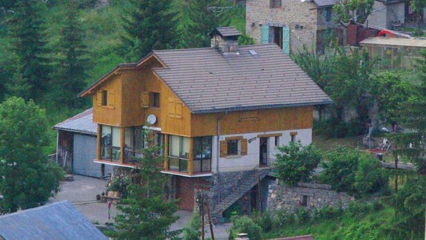A two-story house with a balcony, surrounded by trees.