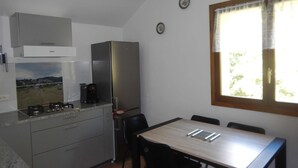 A compact kitchen with a stove, sink, and refrigerator. There is a dining table with chairs and a window with curtains.