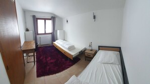 A small, sparsely furnished room with a bed, a desk, a chair, and a radiator.