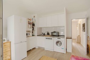 A compact kitchen with a washing machine, microwave, and a small refrigerator.